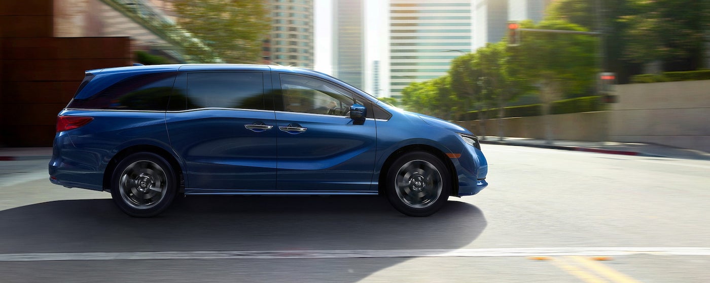 A blue 2023 Honda Odyssey is shown from the side driving on a city street.