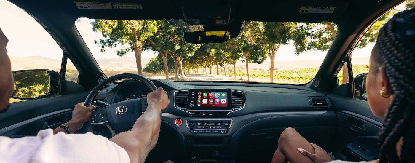 A couple is shown driving a 2023 Honda Passport Trailsport on a dirt road.