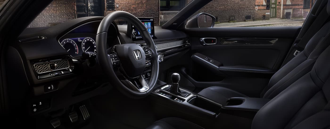 The black interior of a 2024 Honda Civic Hatchback shows the steering wheel and center console.