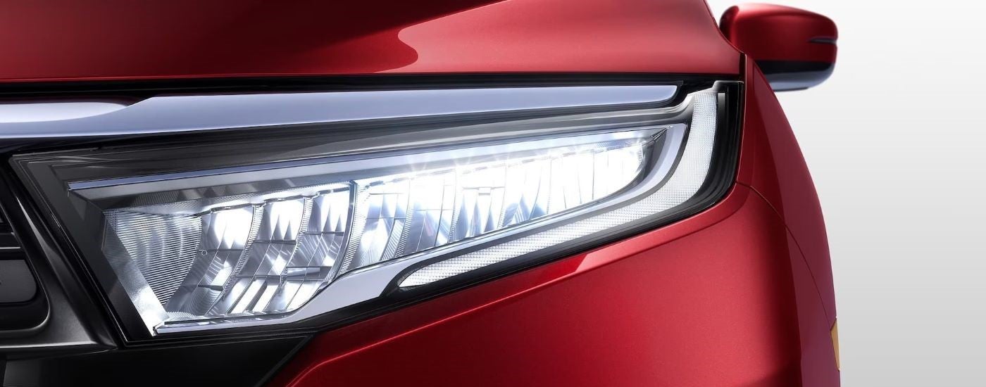 A close up shows the driver side headlight on a red 2024 Honda Odyssey Elite.
