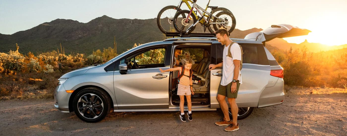 A family is shown next to a 2021 Honda Odyssey van parked near a hiking trail.