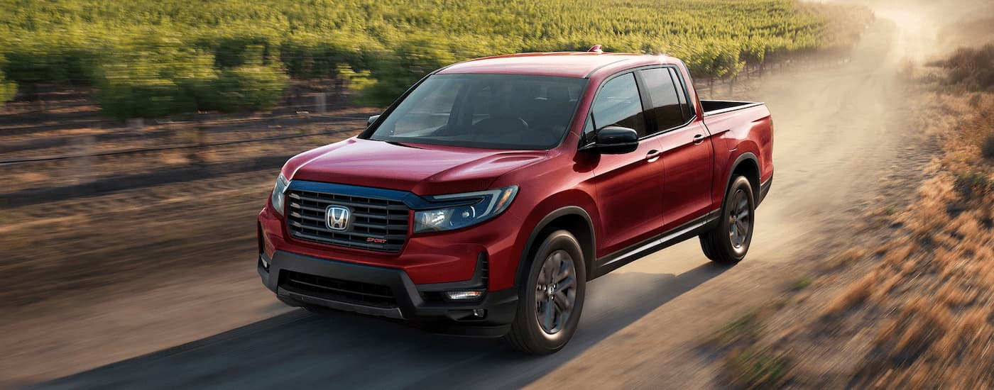 A red 2022 Honda Ridgeline is shown driving on a dirt road.