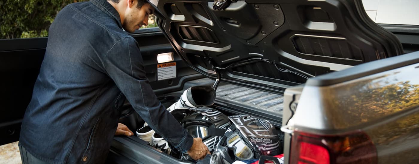 A man is shown putting gear into the bed of a silver 2023 Honda Ridgeline RTL-E.