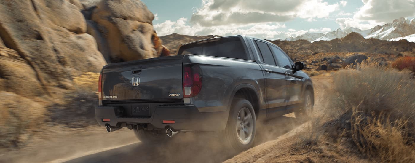 A silver 2023 Honda Ridgeline RTl-E for sale is shown off-roading on a dusty road.