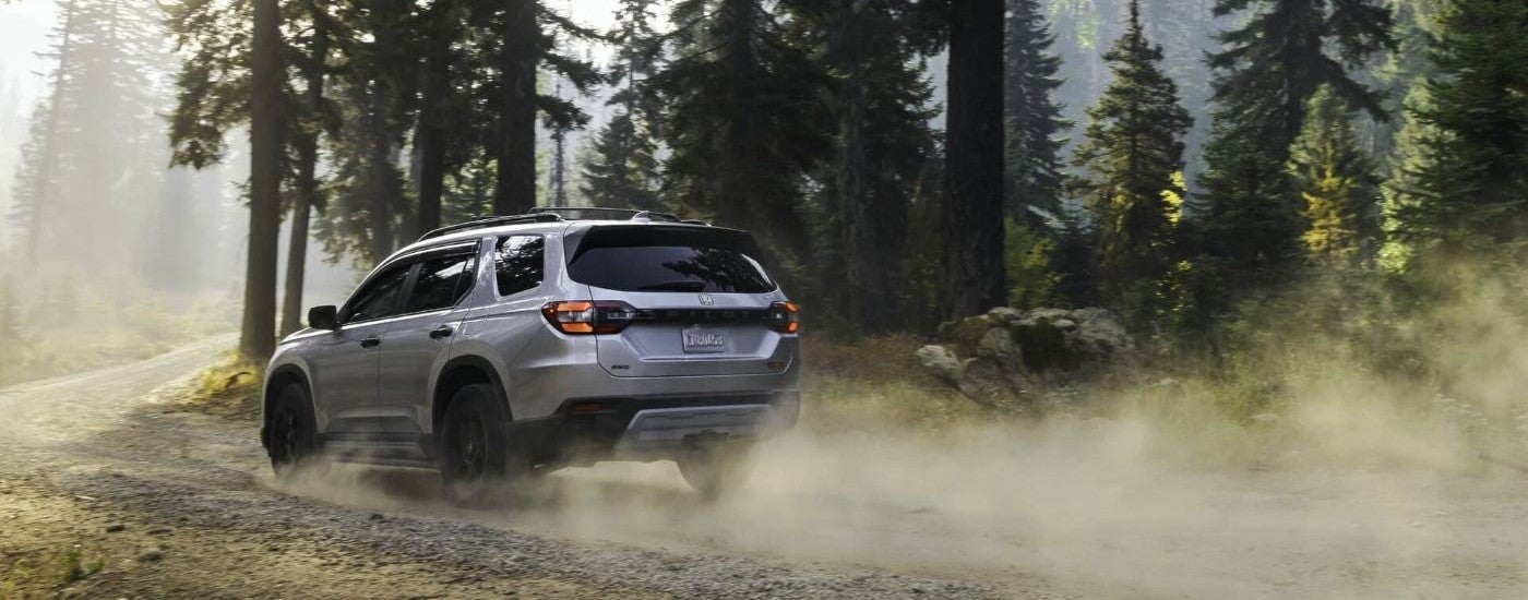 A grey 2023 Honda Pilot Trailsport is shown kicking up dust on a trail.