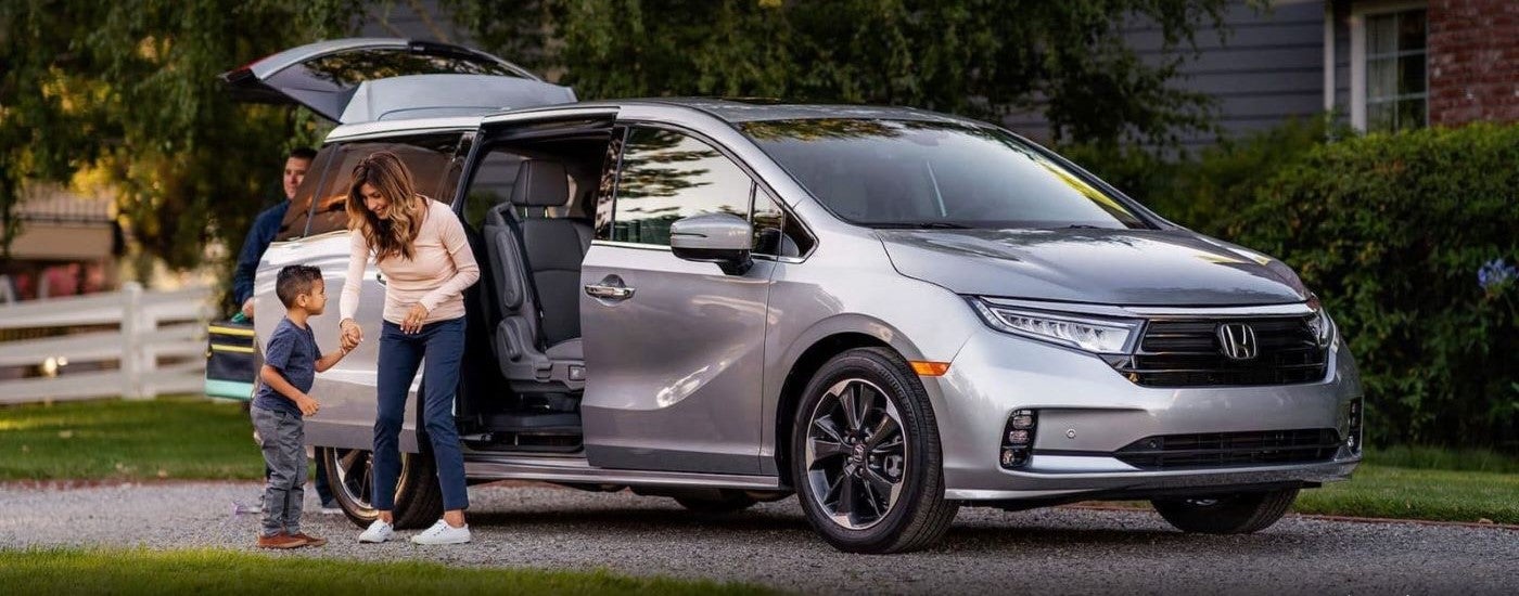 A family is shown next to a silver 2023 Honda Odyssey parked in a driveway.