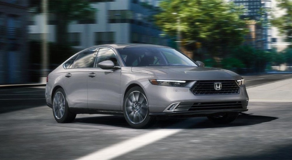 A grey 2023 Honda Accord Touring Hybrid is shown driving through an intersection.