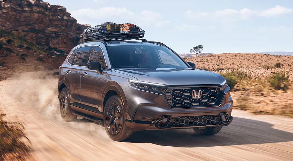 A grey 2023 Honda CR-V is shown driving on a dusty desert road.