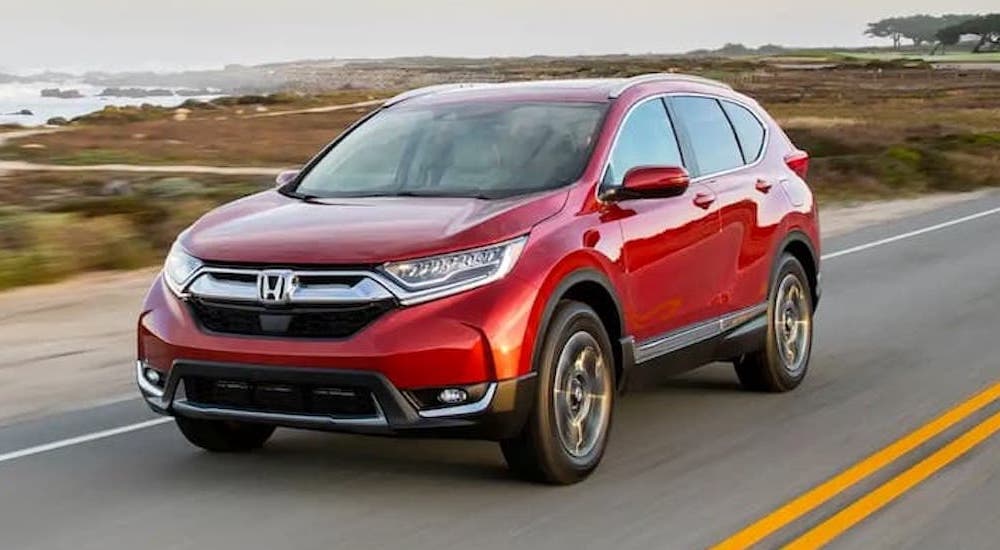 A red 2018 Honda CR-V is shown driving on a highway with an ocean view.