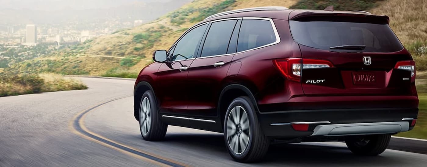 A red 2020 Honda Pilot Touring is shown from a rear angle driving on a winding road after viewing used cars for sale in Midland.