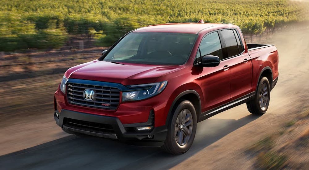 A red 2022 Honda Ridgeline Sport is shown driving on a dusty road after viewing used cars for sale near Odessa.
