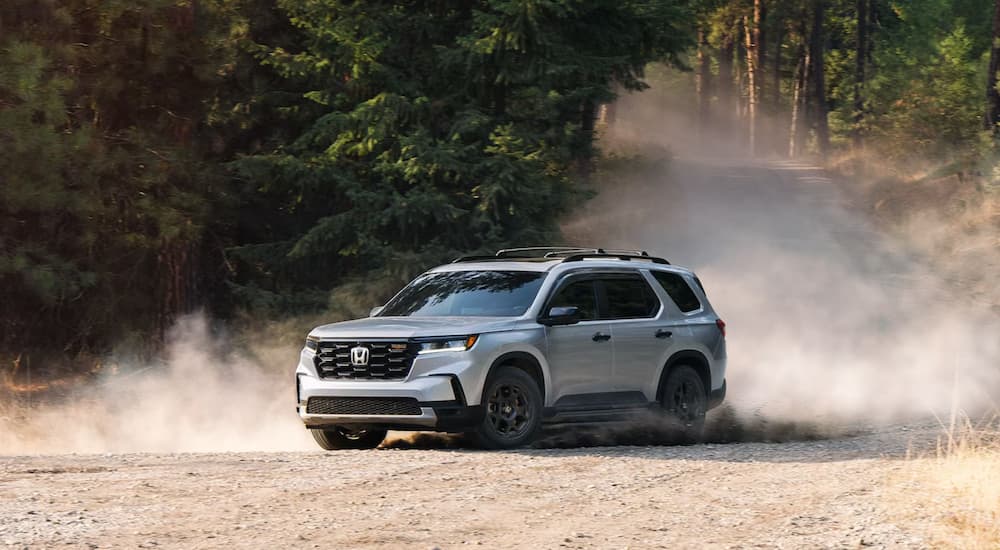A white 2025 Honda Pilot TrailSport kicking up dust on a wooded trail.