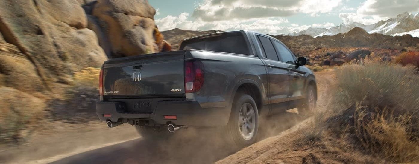 A silver 2022 Honda Ridgeline is shown from the rear driving on a dusty dirt road.