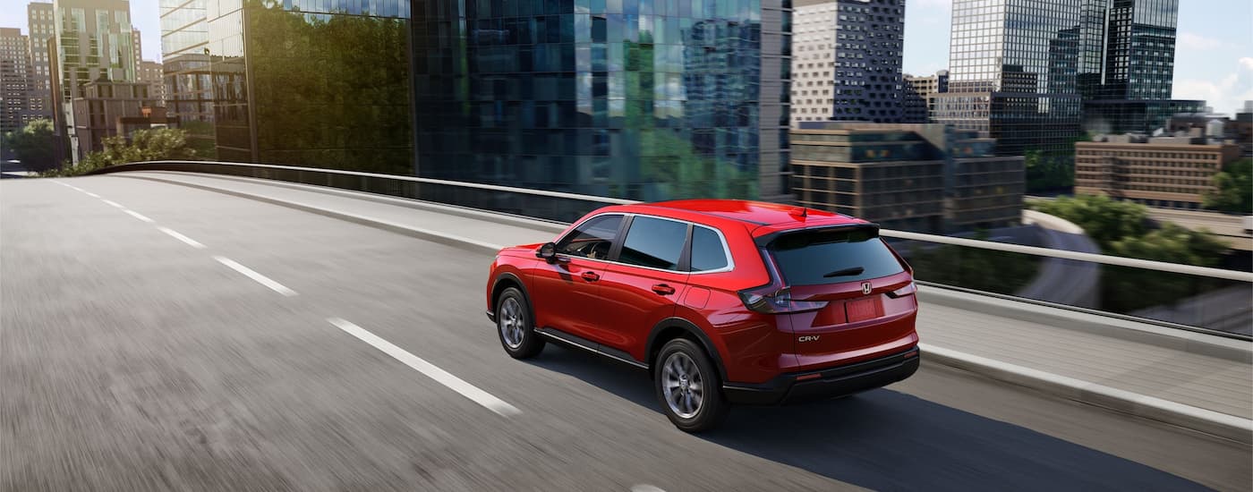 A red 2023 Honda CR-V is shown from a rear angle driving on a highway overpass.
