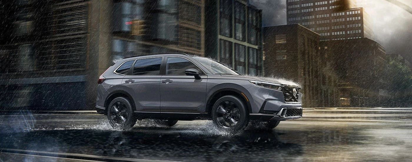 A grey 2023 Honda CR-V Hybrid Sport Touring is shown from the side driving in a city on a rainy day.