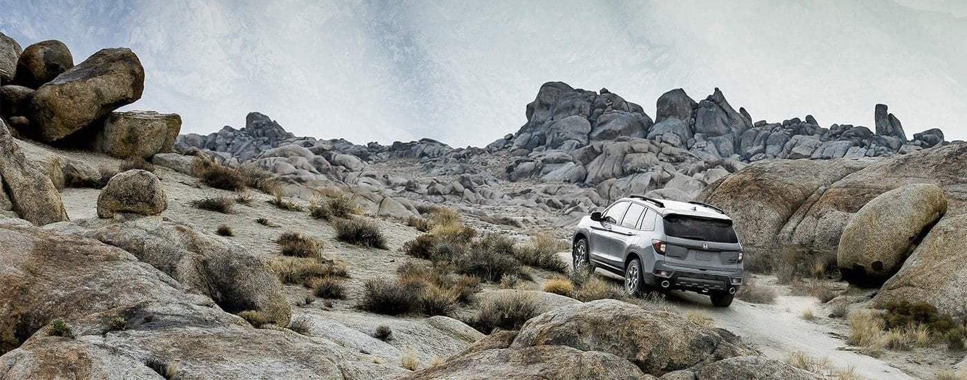 A silver 2023 Honda Passport TrailSport is shown from the rear driving up a mountain trail.
