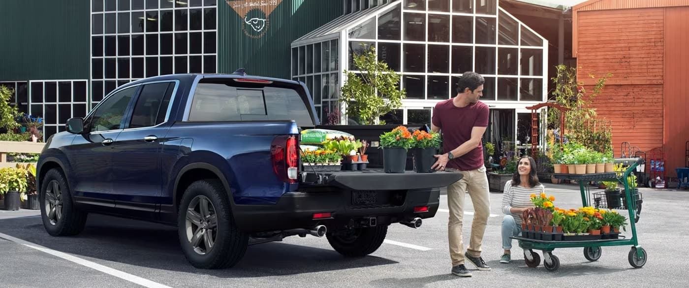 A blue 2023 Honda Ridgeline is shown from a rear angle as a man loads flowers into the bed.