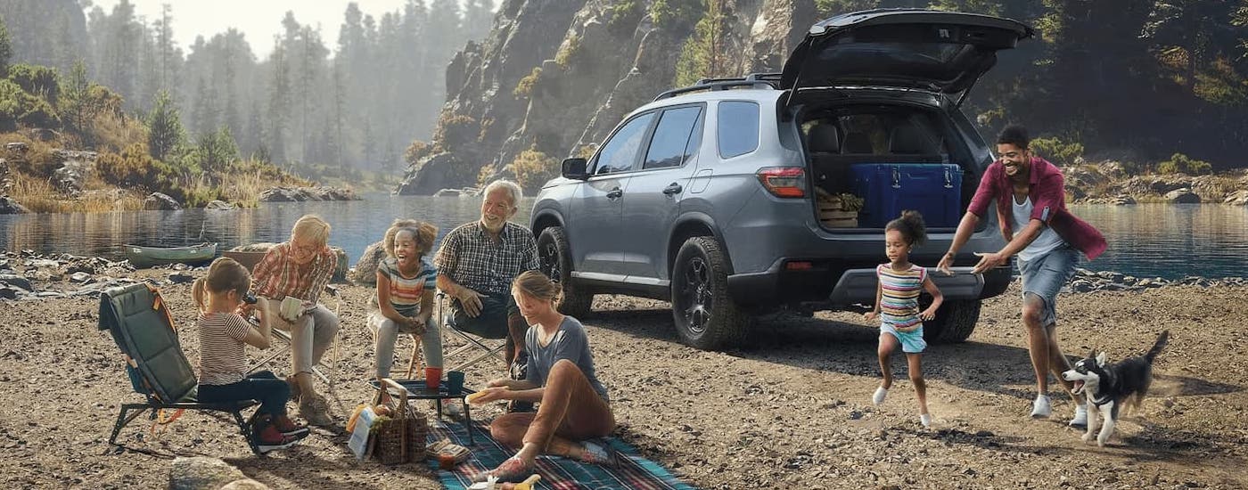 A family is camping next to a grey 2024 Honda Pilot Trailsport on a beach.