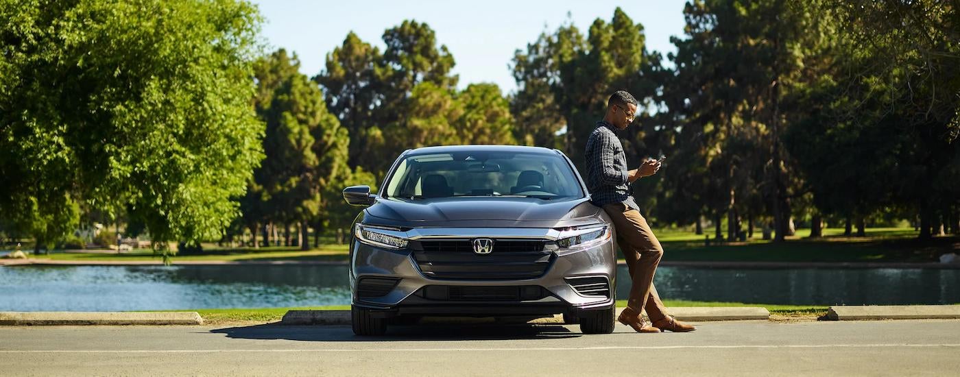 A man in shown leaning against a grey 2022 Honda Insight parked near a small pond.