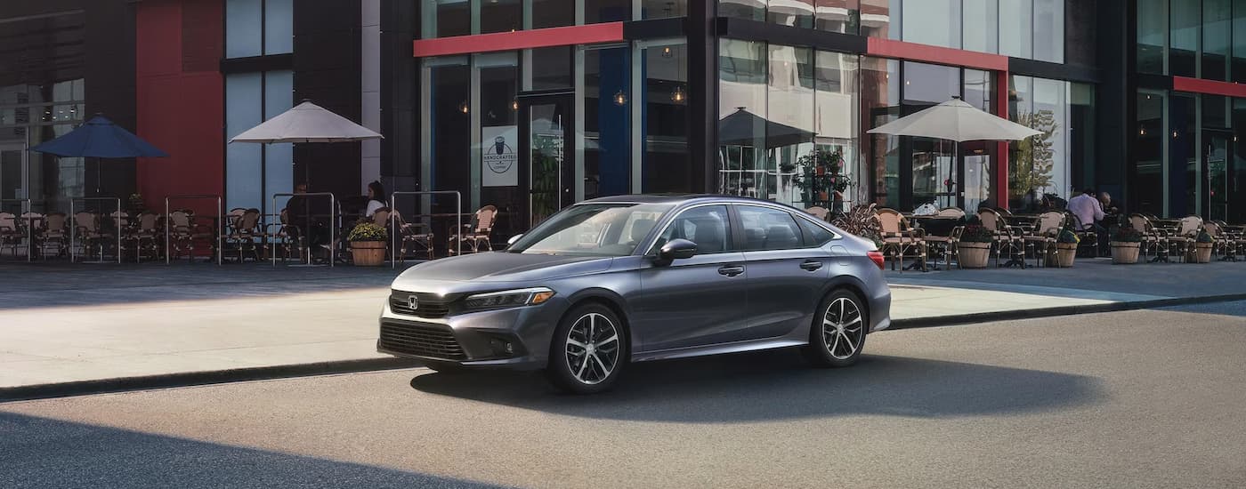 A grey 2024 Honda Civic is shown parked on the side of a city street outside of a cafe.