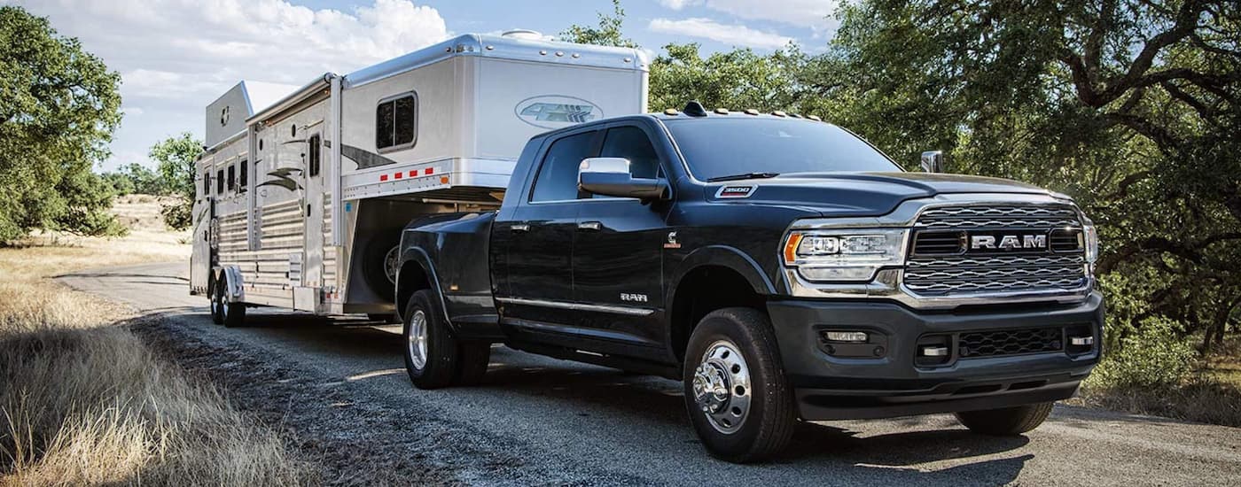 A black 2019 Ram 3500 is shown towing a trailer on a gravel road.