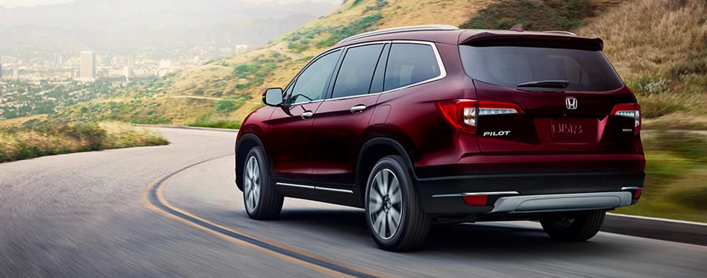 A maroon 2022 Honda Pilot Touring is shown driving toward a city on a curvy road.