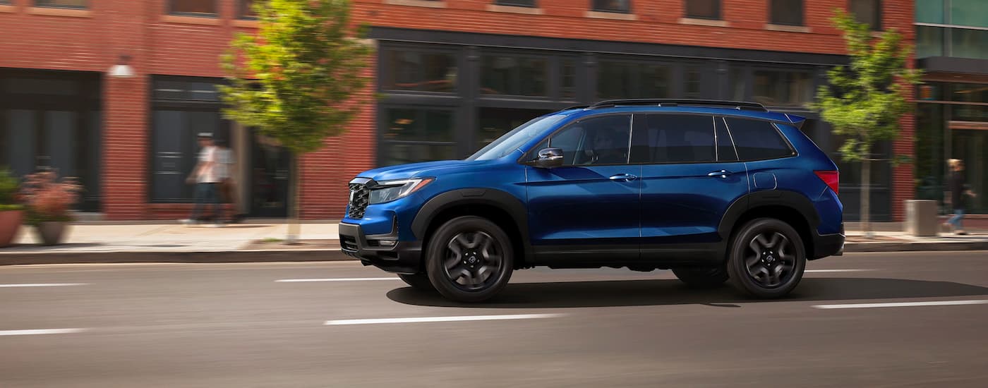 A blue 2021 Honda Passport is shown from the side driving on a city street.