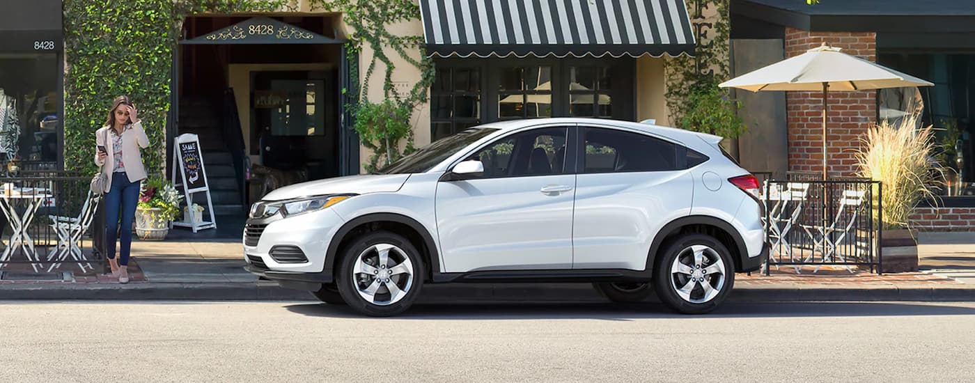 A white 2020 Honda HR-V is shown from the side driving on a city street after viewing used SUVs for sale.