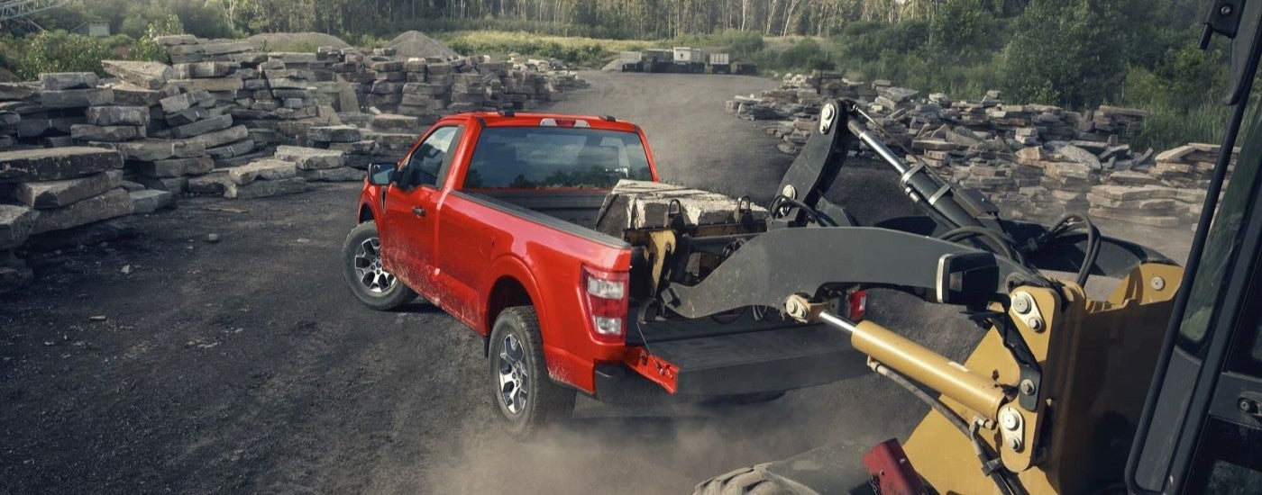 A construction vehicle is shown loading rocks in the bed of a red 2022 Ford F-150 XL.