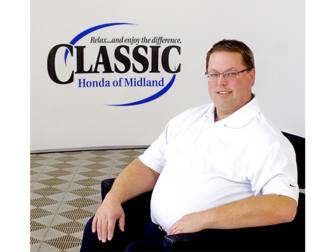 Man in a White Shirt Sitting in a Chair with the Classic Honda of Midland Logo Above Him