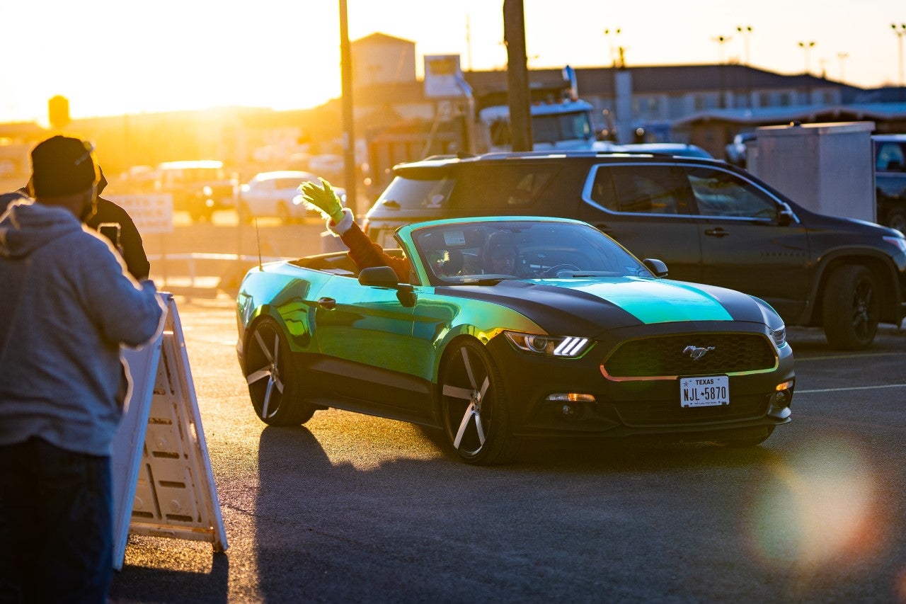 Grinch Waving to a Crowd from the Passenger Seat of a Green and Black Mustang