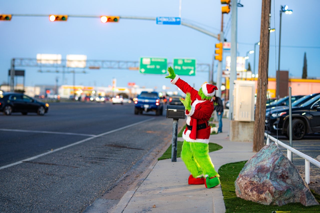Grinch in a Santa Suit Waving to Cars Driving by on the Street